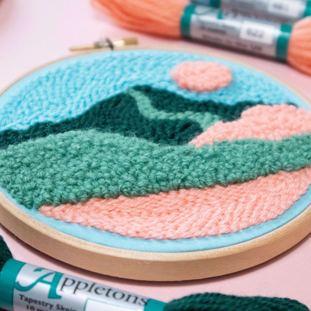 Punch Needle Embroidery hoop with a mountain landscape design and Appletons embroidery floss on a pink background